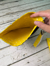 Load image into Gallery viewer, A close-up of a hand holding open a small yellow fabric pouch with white polka dots, showing the interior lining, on a whitewashed wooden surface.