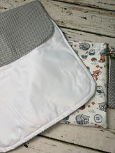 Load image into Gallery viewer, A close-up of a changing pad showing two fabric sides: one side is white with a gray polka-dot folded flap, and the other side features a woodland animal print on a cream background with gray, orange, and blue details.