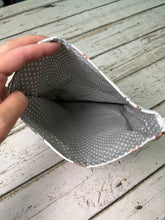 Load image into Gallery viewer, A close-up of a hand holding open a small fabric pouch or bag, showing a gray interior with small white polka dots and a white stitched edge, set against a distressed white wooden surface.