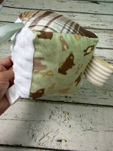 Load image into Gallery viewer, A handmade baby sensory cube being held by a hand, featuring a light green fabric panel with a brown bear pattern, a white textured fabric panel, a brown plaid fabric panel, and striped fabric tabs.