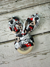 Load image into Gallery viewer, A fabric baby teether with a wooden ring handle, featuring a bunny ear shaped top printed with a Mickey Mouse pattern on a weathered white wood background.