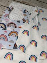 Load image into Gallery viewer, Two fabric baby bibs laid flat on a rustic wooden surface. One bib has a white background with a colorful rainbow and cloud print, and the other shows a dotted pattern on the reverse side.
