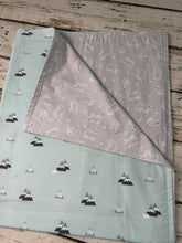 Load image into Gallery viewer, A folded baby blanket with a dual-pattern design, featuring a light mint green side with black and white mountain prints and a light gray side with white polar bear outlines, displayed on a rustic wooden surface.