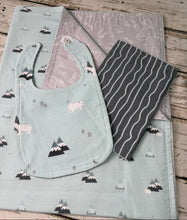 Load image into Gallery viewer, A baby gift set laid flat on a rustic wooden surface, including a pale mint bib with polar bear and mountain prints, a matching blanket in pale mint and gray, and a dark gray burp cloth with wavy mint lines.