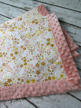 Load image into Gallery viewer, A folded baby blanket with a pink minky dot border and a white center printed with small pink, yellow, and gold flowers, displayed on a rustic white wooden surface.
