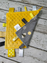 Load image into Gallery viewer, A baby sensory lovey blanket featuring a yellow minky dot fabric back and a gray fabric beea and honeycomb design, decorated with colorful ribbon tabs on a rustic white wood background.
