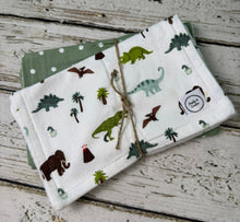 Load image into Gallery viewer, A stack of two reusable cloth baby wipes tied with twine, featuring a white top layer with a colorful dinosaur and palm tree print, and a sage green polka dot underneath, displayed on a rustic white-washed wooden surface.
