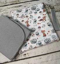 Load image into Gallery viewer, A fabric pouch with a woodland animal print featuring foxes, owls, and hedgehogs on a white background, shown alongside a matching gray polka-dot pouch on a rustic wooden surface.
