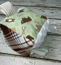 Load image into Gallery viewer, A small fabric sensory cube with a woodland bear print on a light green panel, a brown plaid side panel, white ruffled trim, and ribbon pulls, photographed on a distressed white wood surface.

