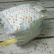 Load image into Gallery viewer, A handmade baby sensory cube toy with a pale green fabric top printed with dinosaurs, a gray minky dot side, a gray patterned ribbon loop
