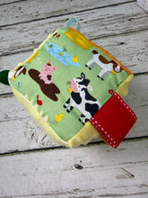Load image into Gallery viewer, A square toy with a colorful farm animal print on a light green background, featuring ribbons
