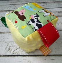 Load image into Gallery viewer, A square toy with a colorful farm animal print on a light green background, featuring ribbons
