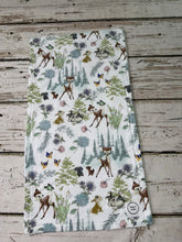 Load image into Gallery viewer, A burp cloth with a Bambi woodland animal print, featuring deer, rabbits, squirrels, and butterflies among trees and flowers on a white background, laid flat on a rustic wooden surface.
