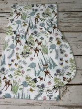 Load image into Gallery viewer, A burp cloth and bib with a Bambi woodland animal print, featuring deer, rabbits, squirrels, and butterflies among trees and flowers on a white background, laid flat on a rustic wooden surface.
