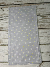 Load image into Gallery viewer, A burp cloth covered in a small white and yellow daisy pattern, laid flat on a rustic white-washed wooden surface.
